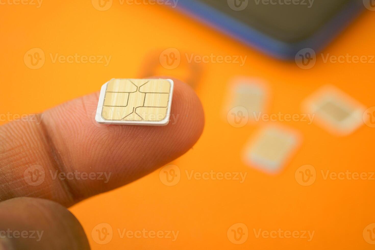 SIM card in fingers, others behind on orange surface photo
