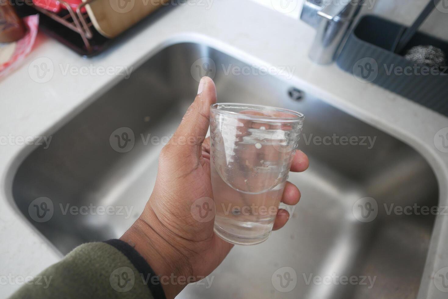 dirty Glass of water held above kitchen sink photo