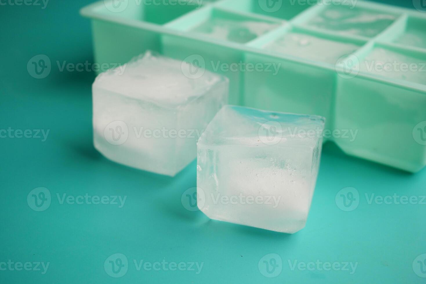 Ice cubes resting beside a green ice tray on a bright surface photo