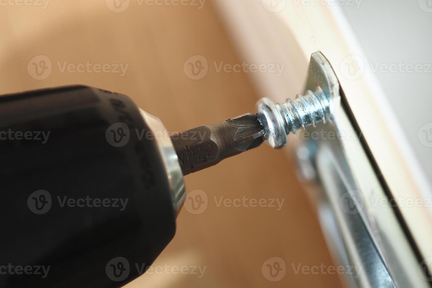 Close-up of a drill fastening a screw into wood material photo