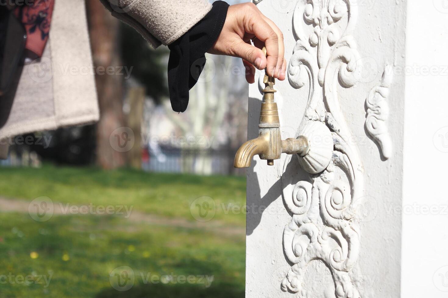 Hand turns vintage faucet in a park on a sunny day photo