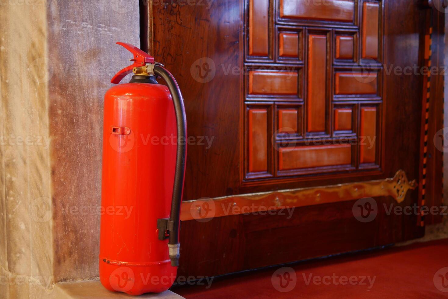 Fire extinguisher placed near wooden door in public building photo