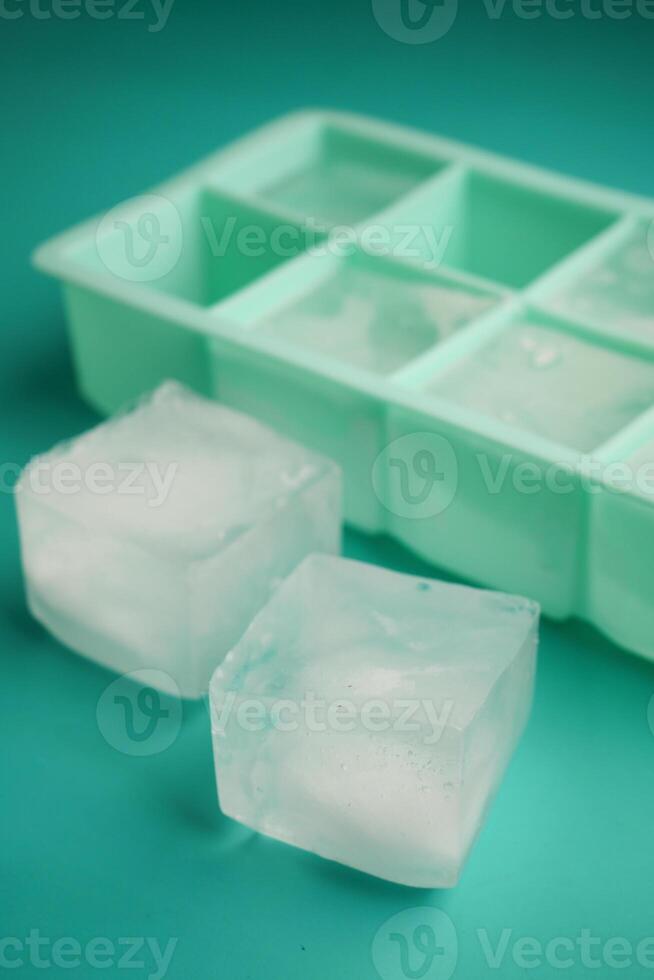 Ice cubes and tray on teal surface with two cubes separated photo