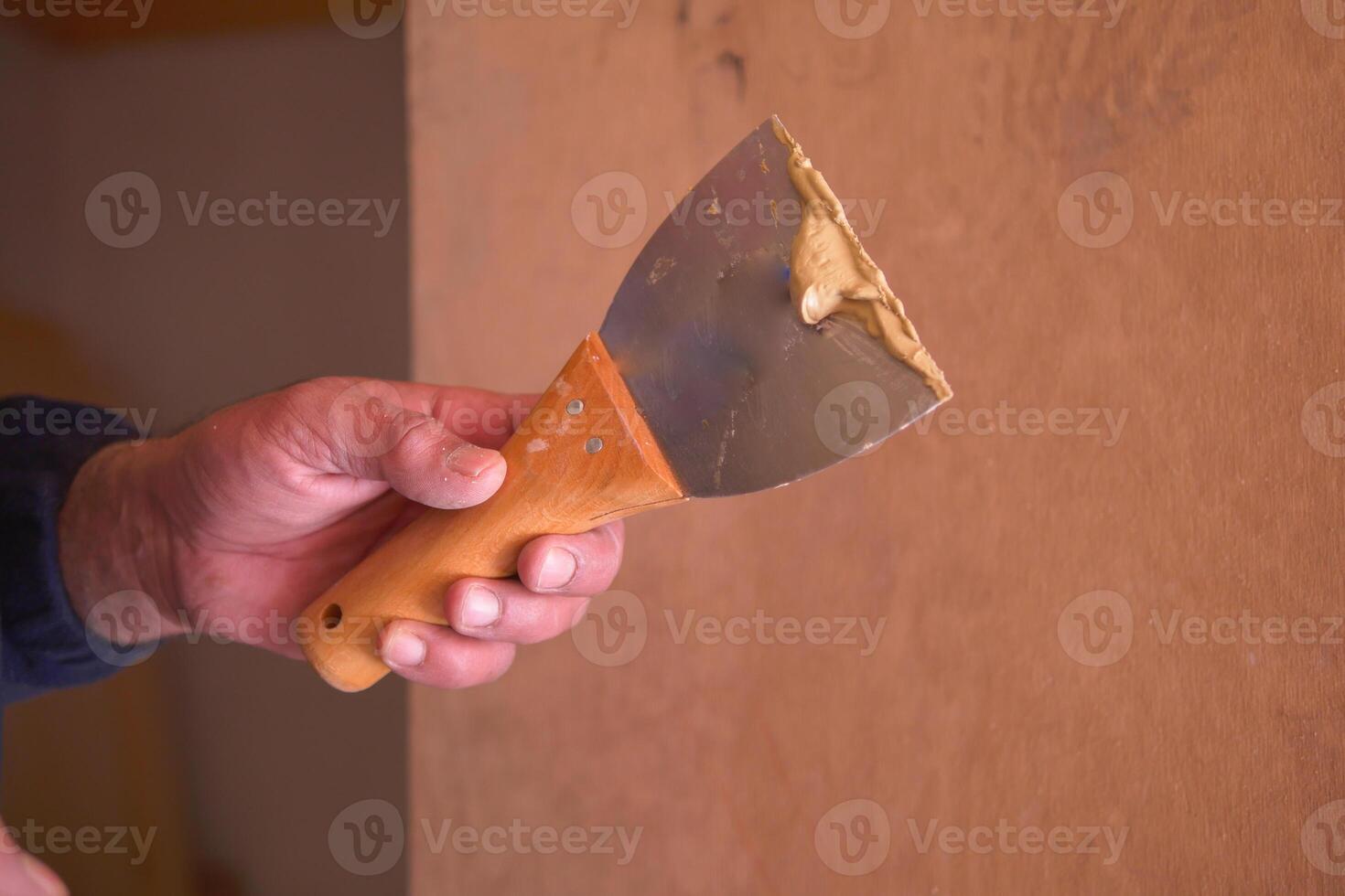 Skilled worker applies putty with a knife to a wood surface photo