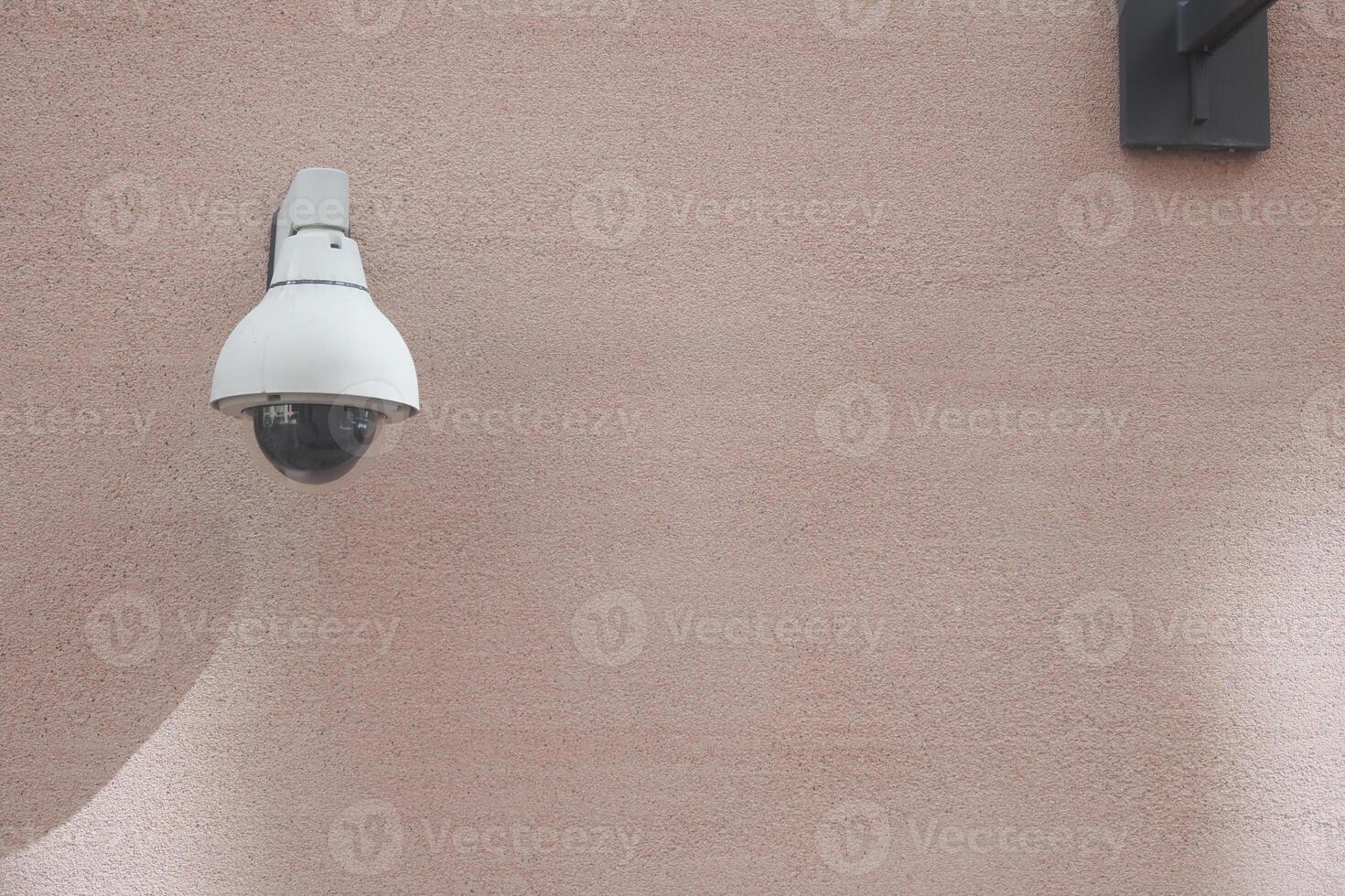 Security camera mounted on a beige wall for monitoring purposes photo