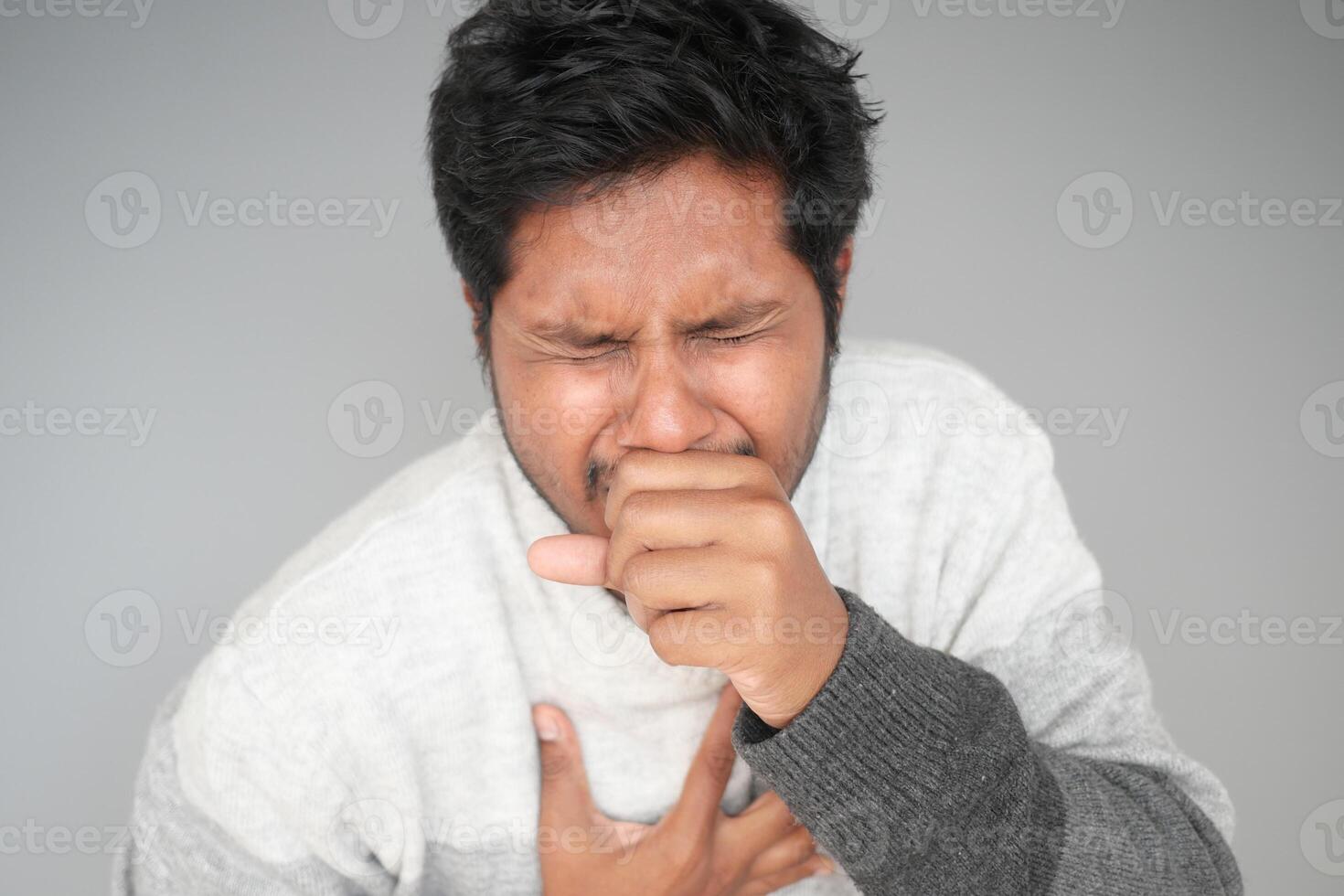 Man experiencing discomfort holding his chest in gray sweater photo
