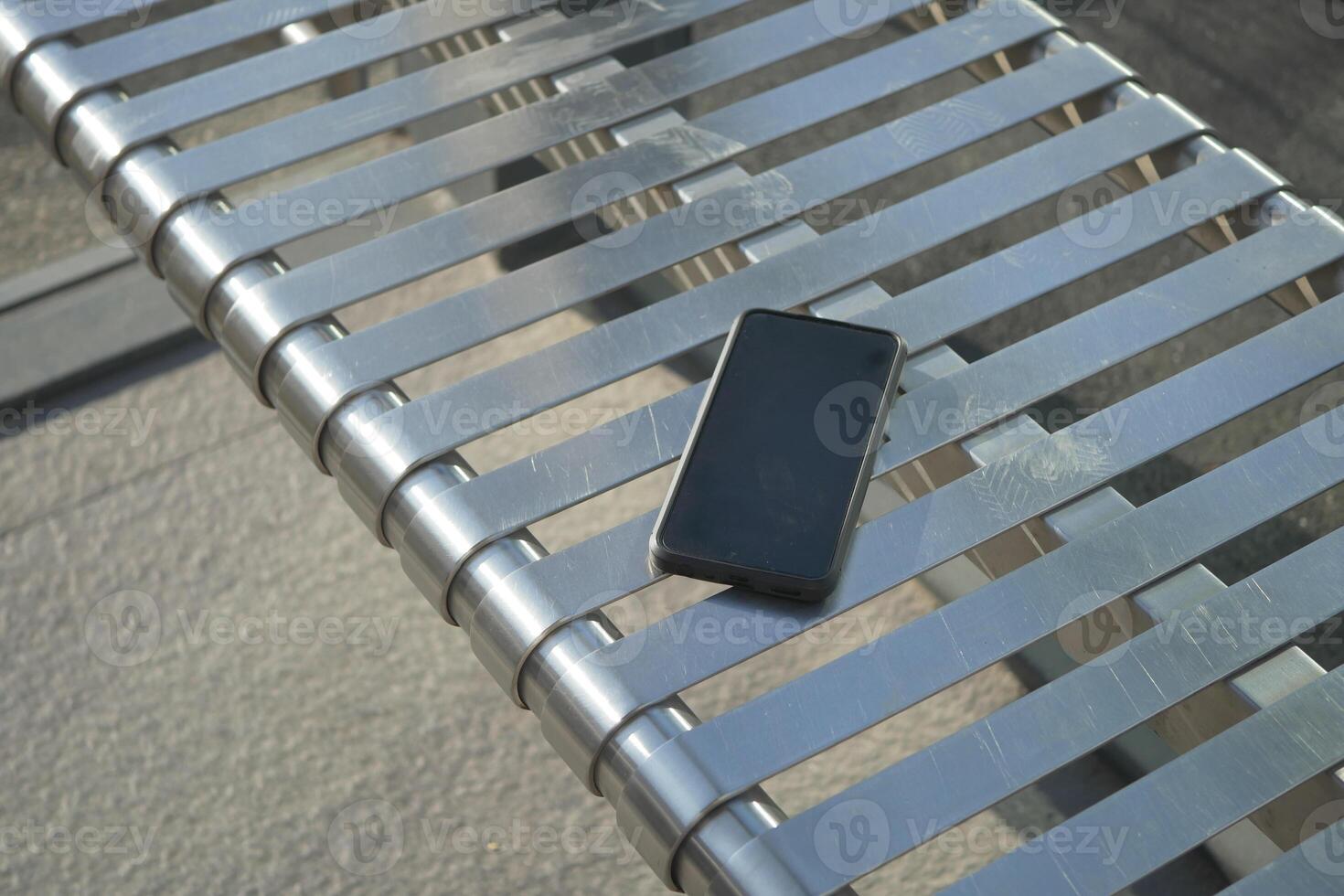 Smartphone resting on a metallic bench.lost smart phone concept photo