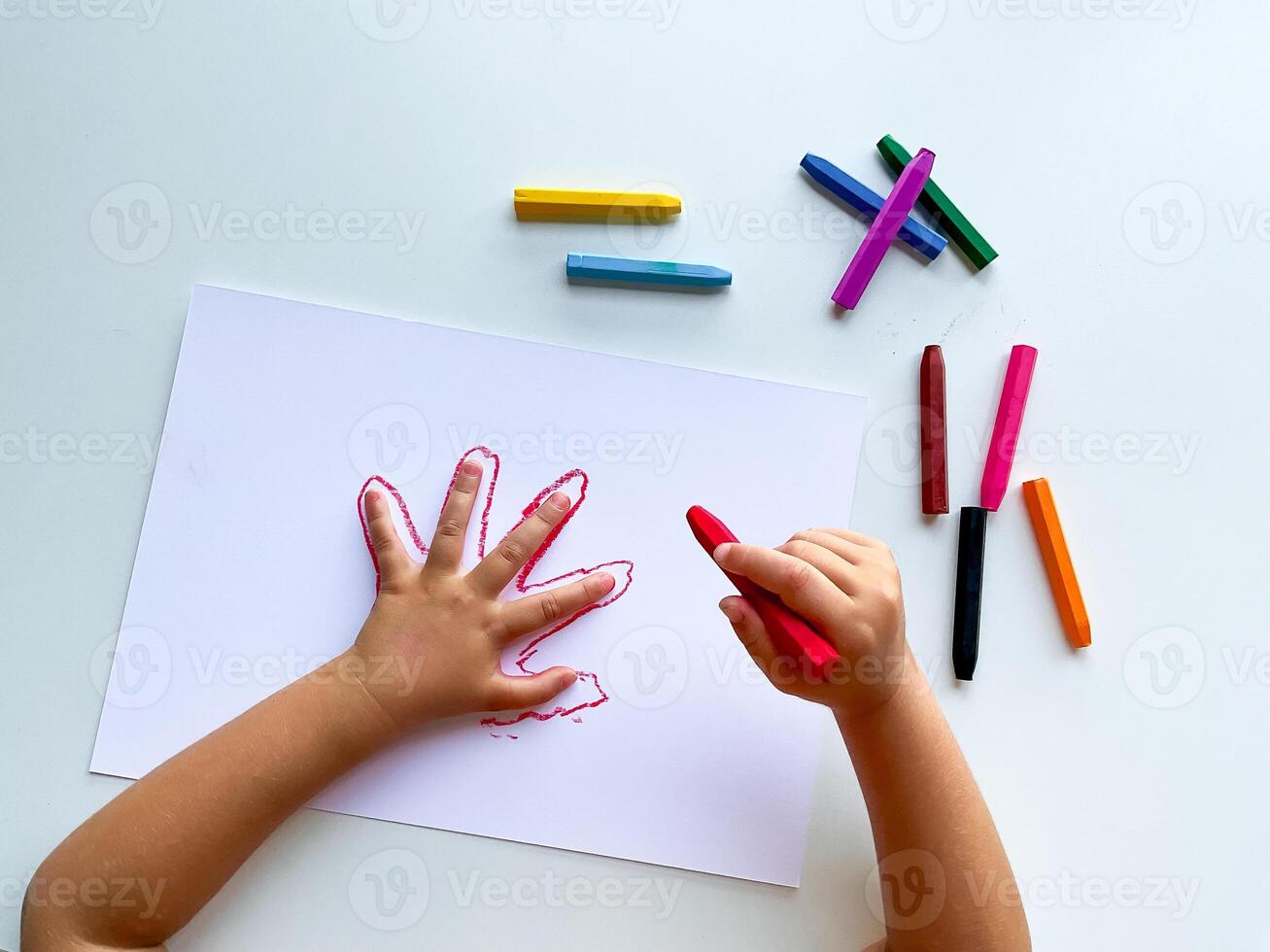 Child drawing hand outline with colorful crayons on white paper photo