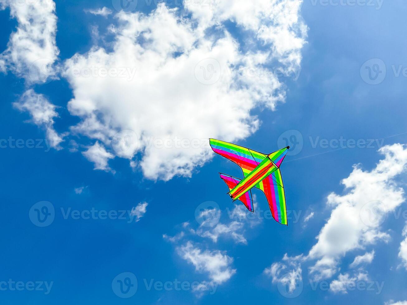 Colorful rainbow kite flying in a clear blue sky with fluffy clouds photo