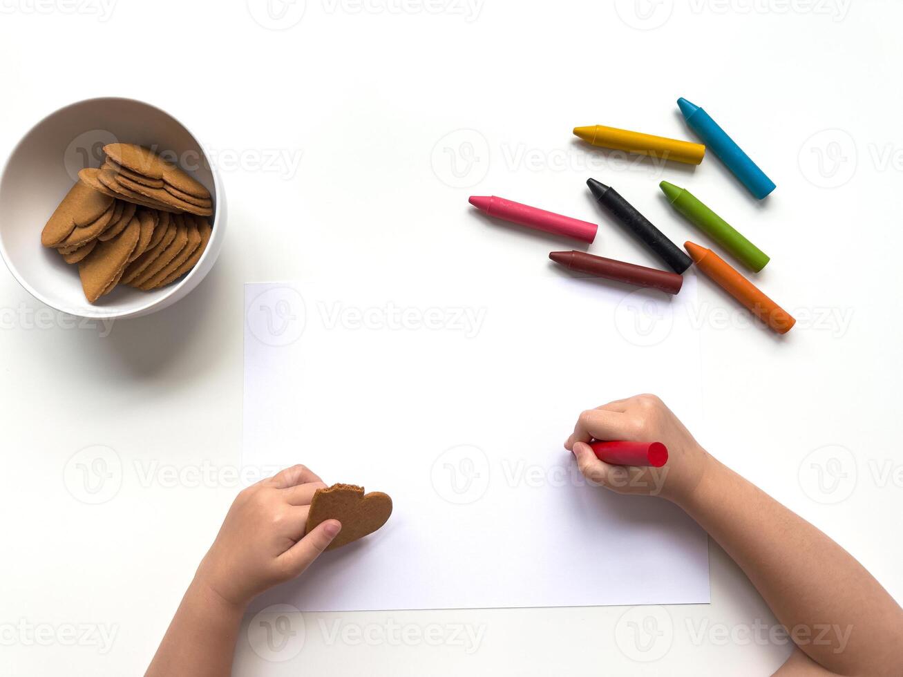 Child drawing with crayons and eating cookies on a white surface photo