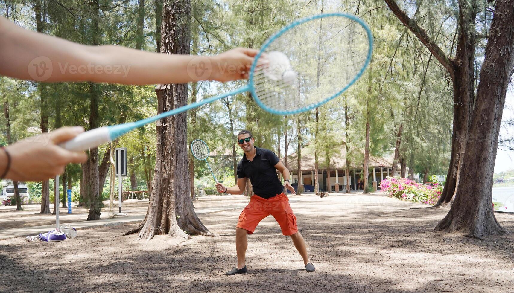 A man and a young woman are playing badminton together in a park photo