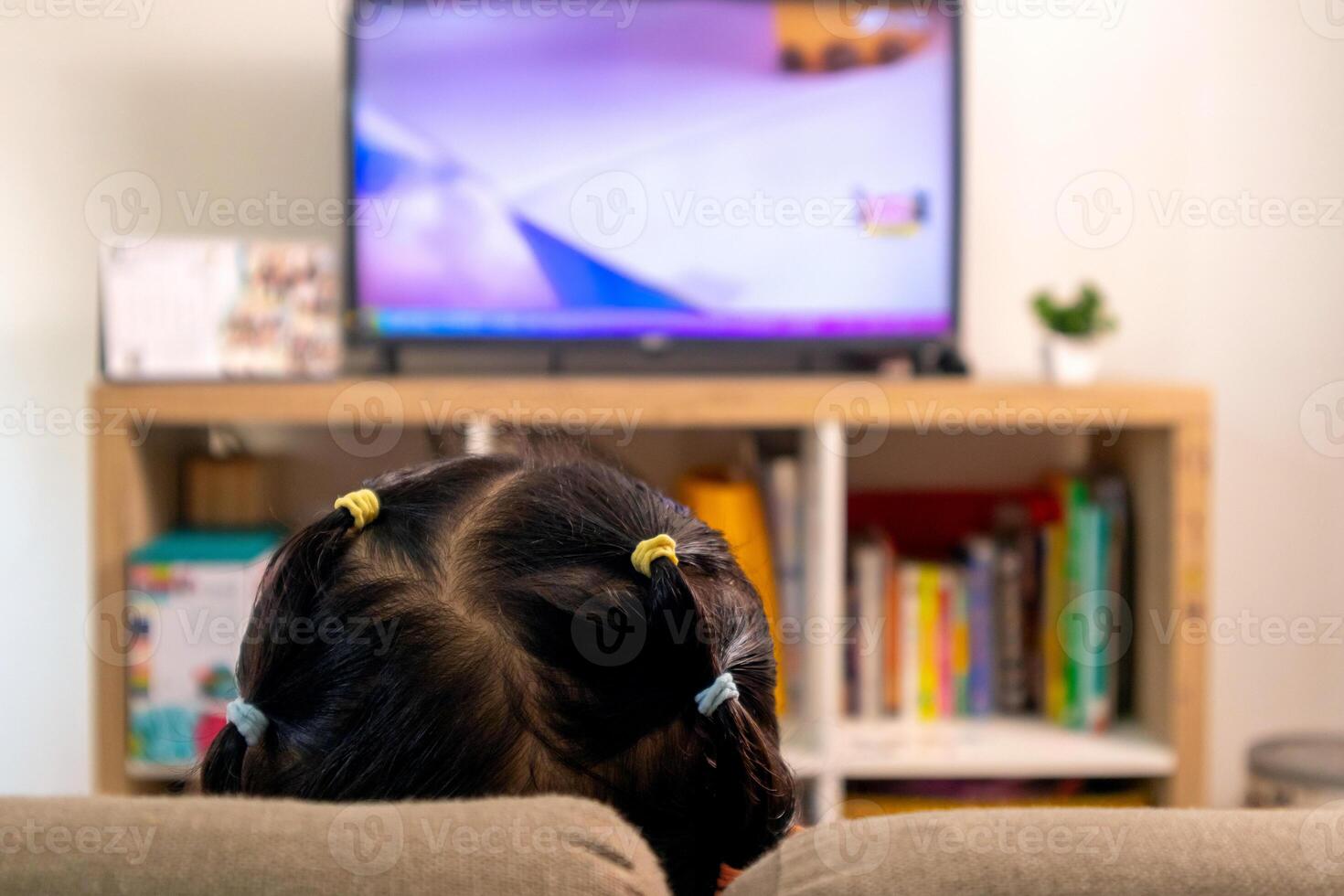 A little girl with with ponytail hair relaxing on sofa while watching the TV at home photo