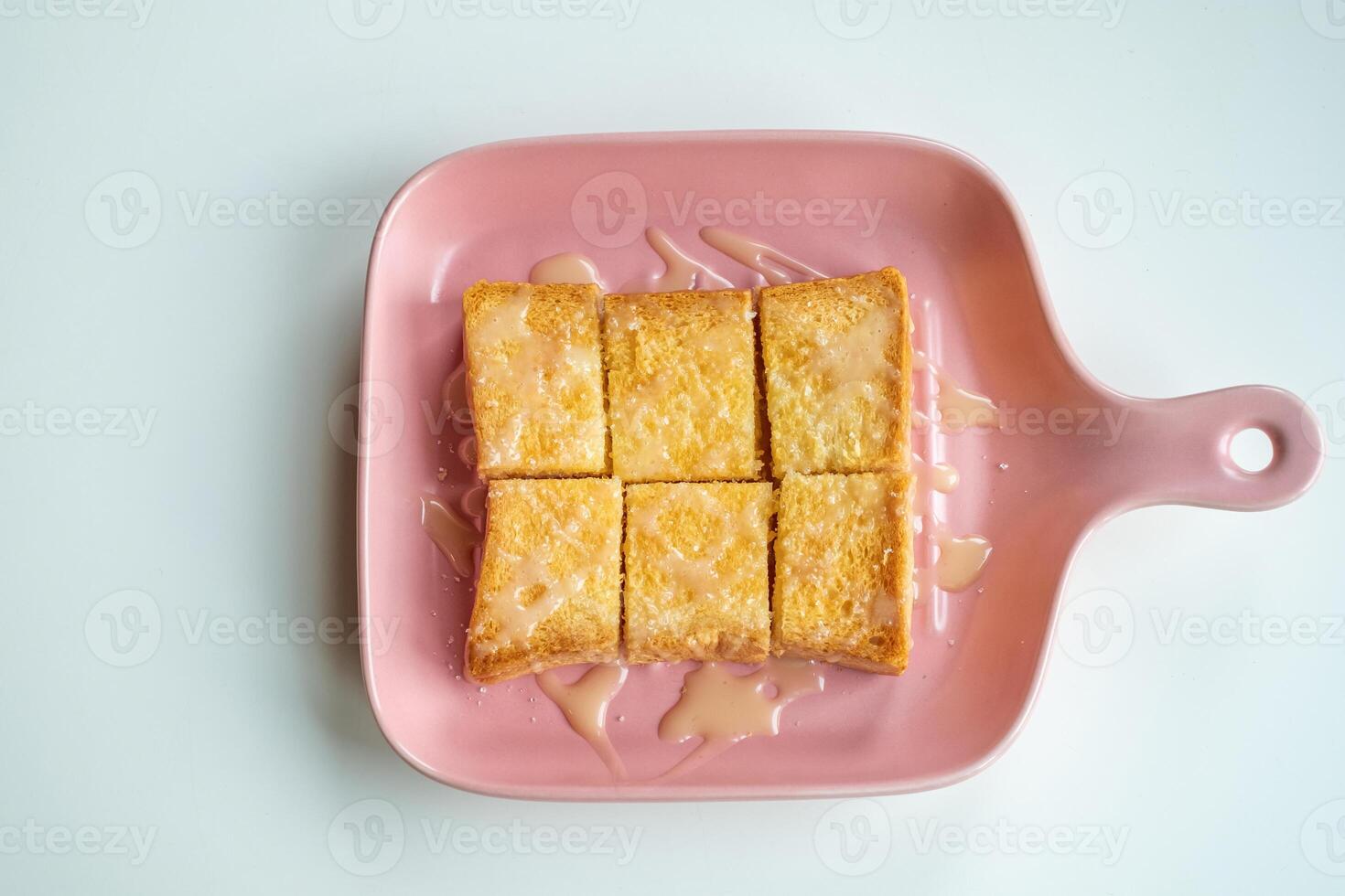 Top view of sliced butter toast with sweet condensed milk drizzled on top, served on a pink plate. Delicious dessert snack presented on a clean white background, minimal and appetizing style photo
