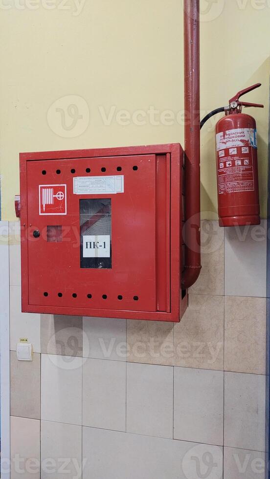 Fire safety cabinet with fire hose and mounted extinguisher on tiled wall inside public supermarket. Concept of fire protection, emergency equipment is store. Vertical photo