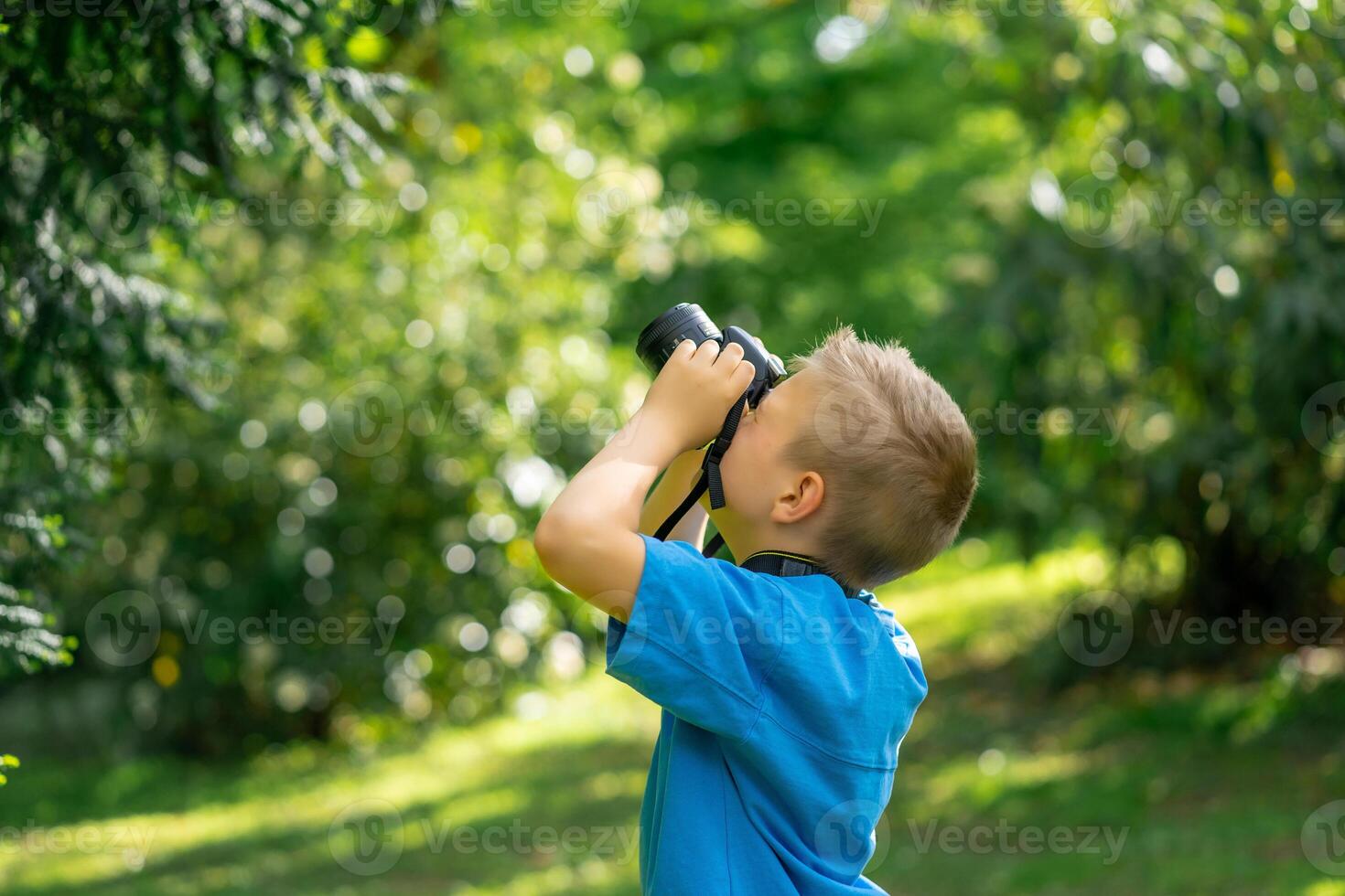 Cute boy in a blue T-shirt takes pictures with the camera in the park photo