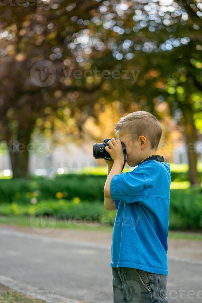 Cute boy in a blue T-shirt takes photos with a camera in a city park