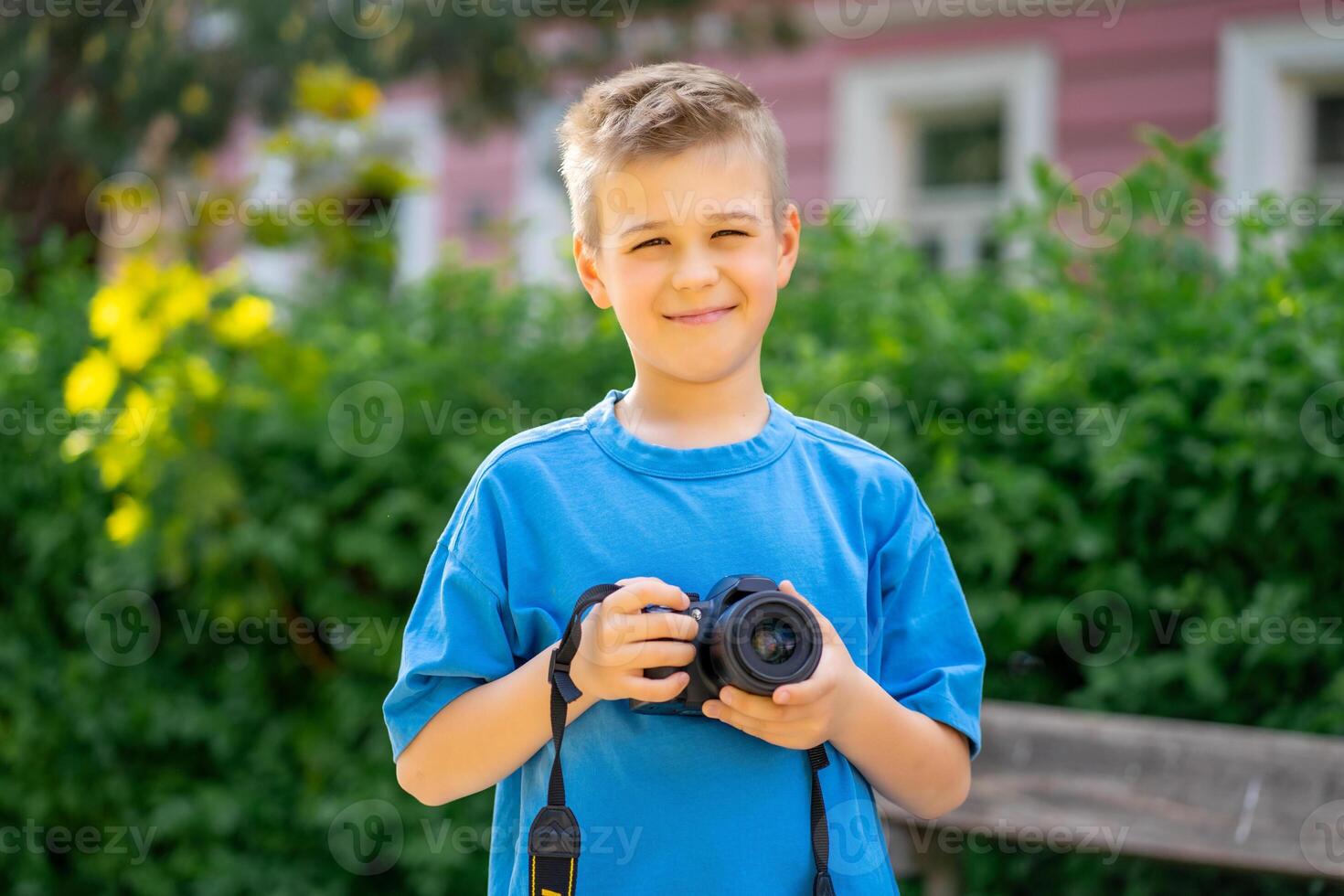 Cute boy in a blue T-shirt holds a digital camera in his hands and smiles photo