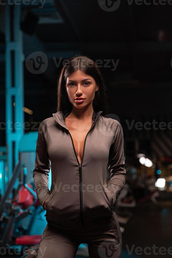 fitness model confidently poses in sleek athletic wear within contemporary gym setting. vibrant lighting enhances energetic atmosphere showcasing dedication fitness and health photo