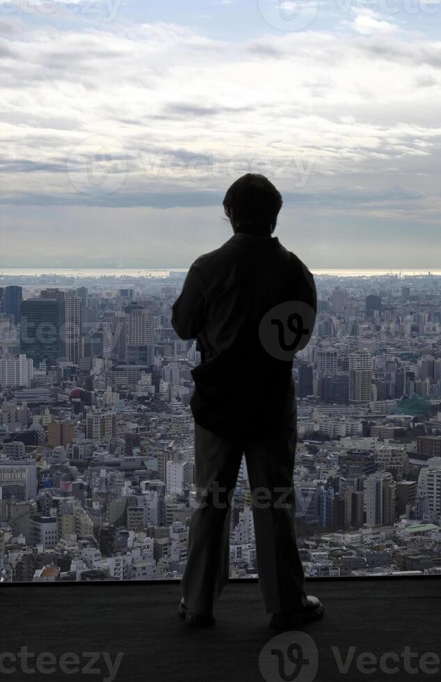 Silhouette of a man standing in front of a window with the skyline of Tokyo in the background photo