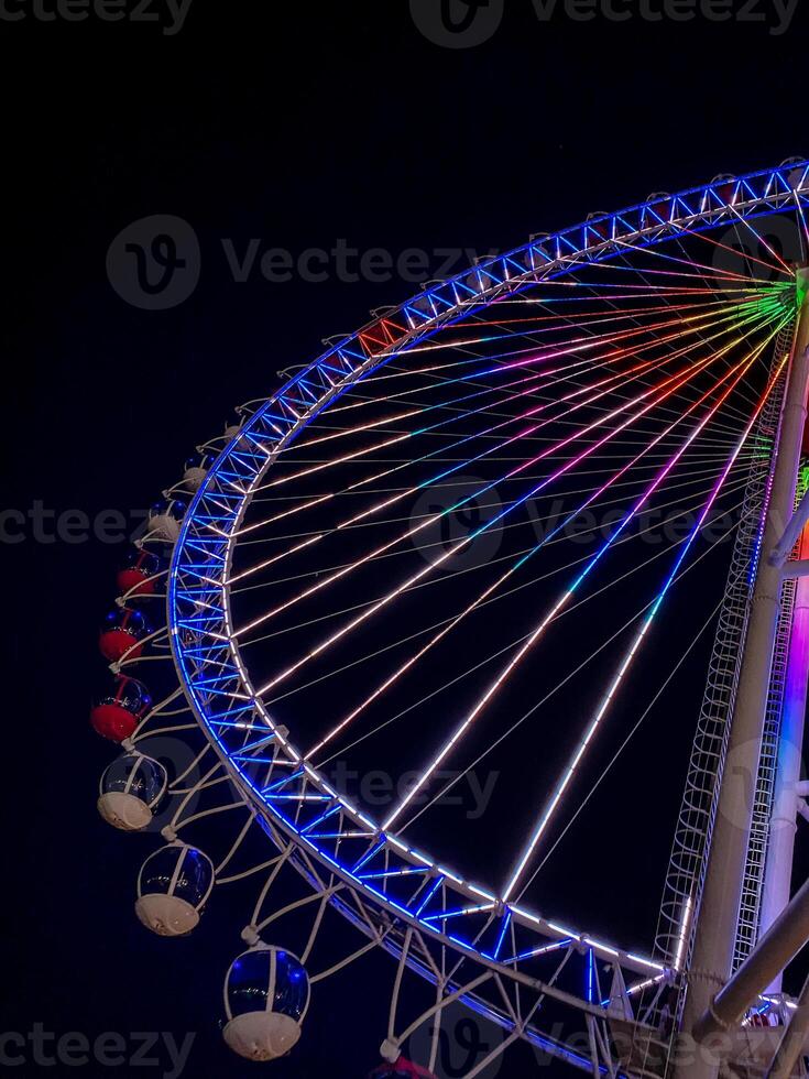 Bright illuminated ferris wheel with colorful neon lights against a dark night sky, creating a vibrant and festive atmosphere perfect for travel, leisure, celebrations, and entertainment themes photo