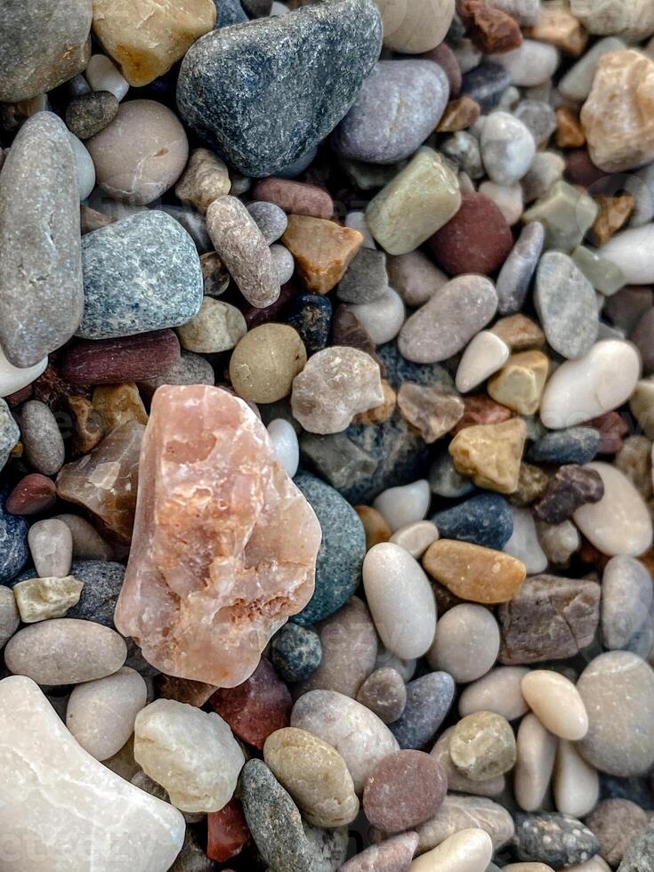 Close-up of colorful beach pebbles with a rough pink mineral rock in the center surrounded by smooth stones of different shapes and earthy tones, creating a vibrant natural background photo