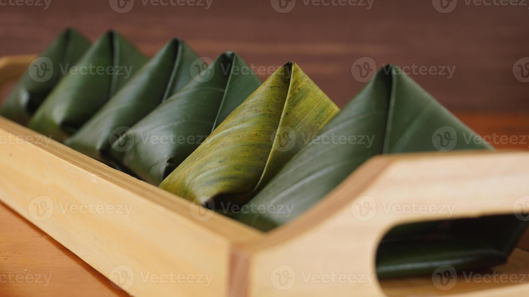 Selective focus of traditional Indonesian snack dessert wrap in green leaves called Kue Bugis on wooden tray photo