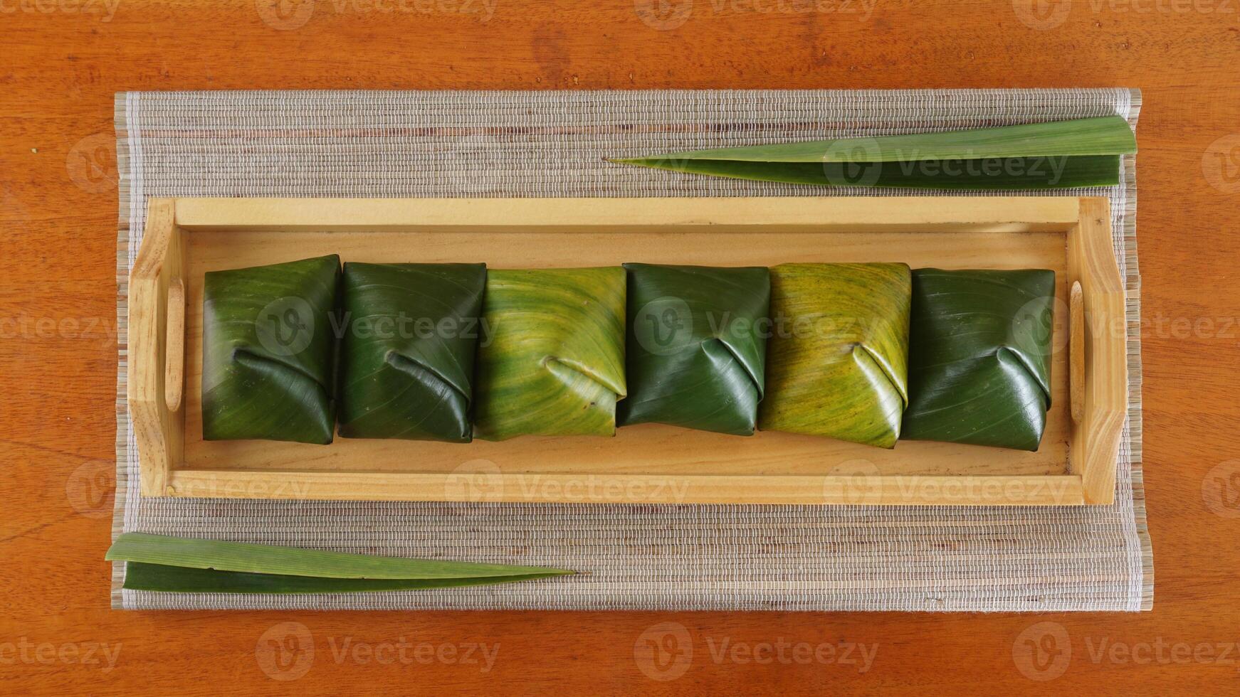 Top view of Kue Bugis, popular traditional dessert snack in Indonesian wrap in green leaves called on wooden tray photo