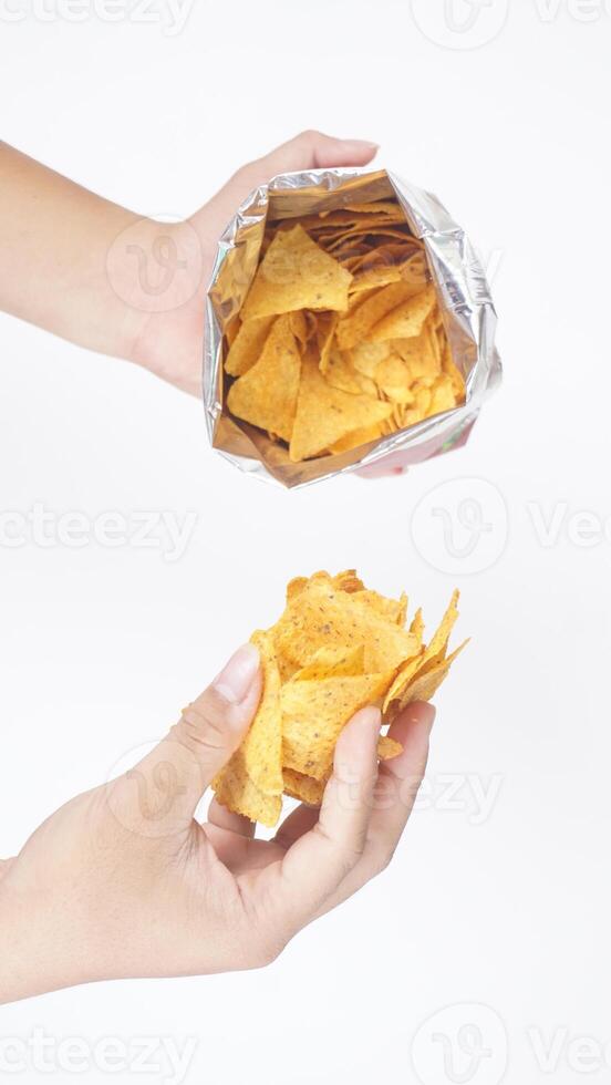 Man hand holds a bunch yellow tortilla chips from opened foil bag isolated on white background photo