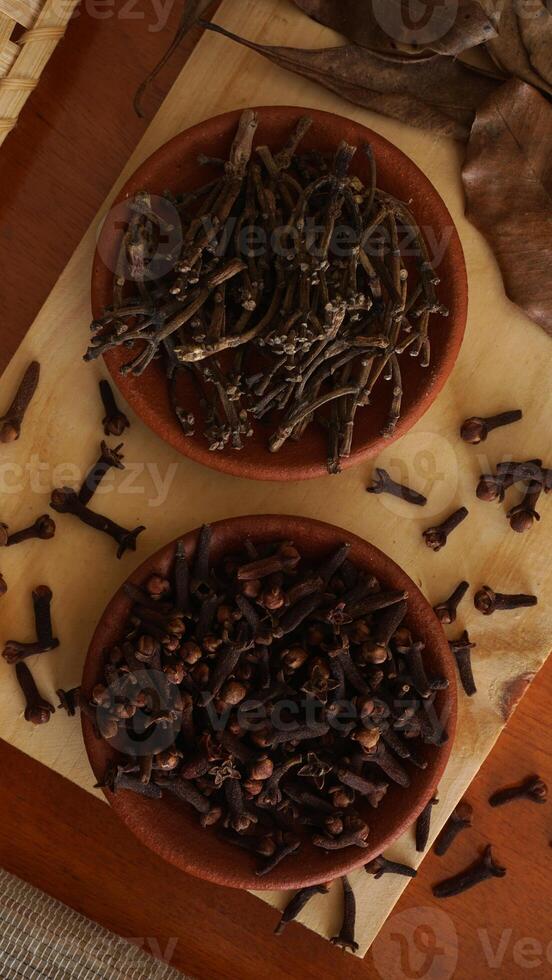Top view of dried cloves spice with dried leaves on wooden platters isolated on wooden texture background photo