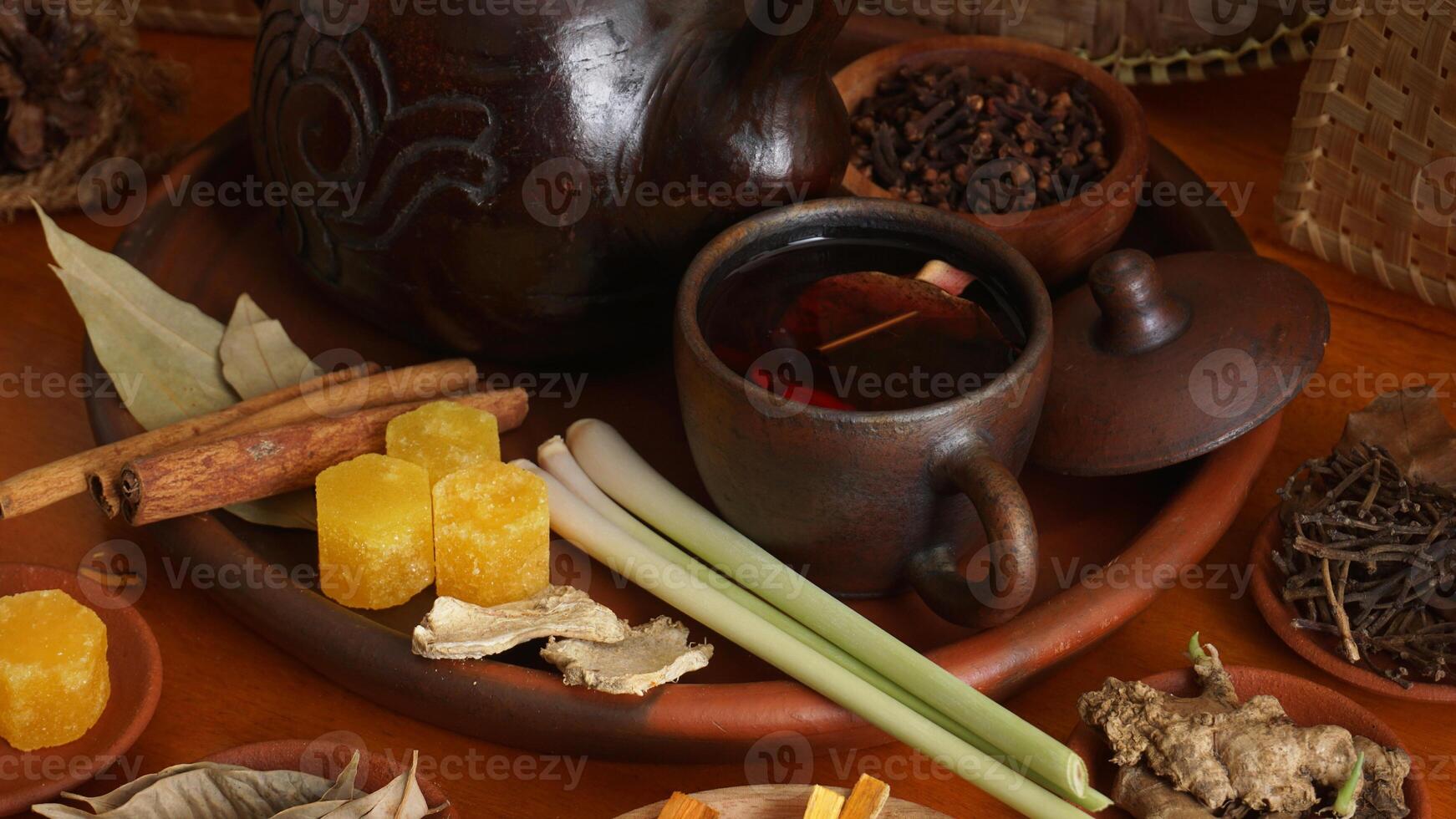 Wedang Uwuh on pottery tea cup with its composition that consist of sappan wood, cinnamon, ginger, lemongrass, and pala leaves, on pottery tray photo