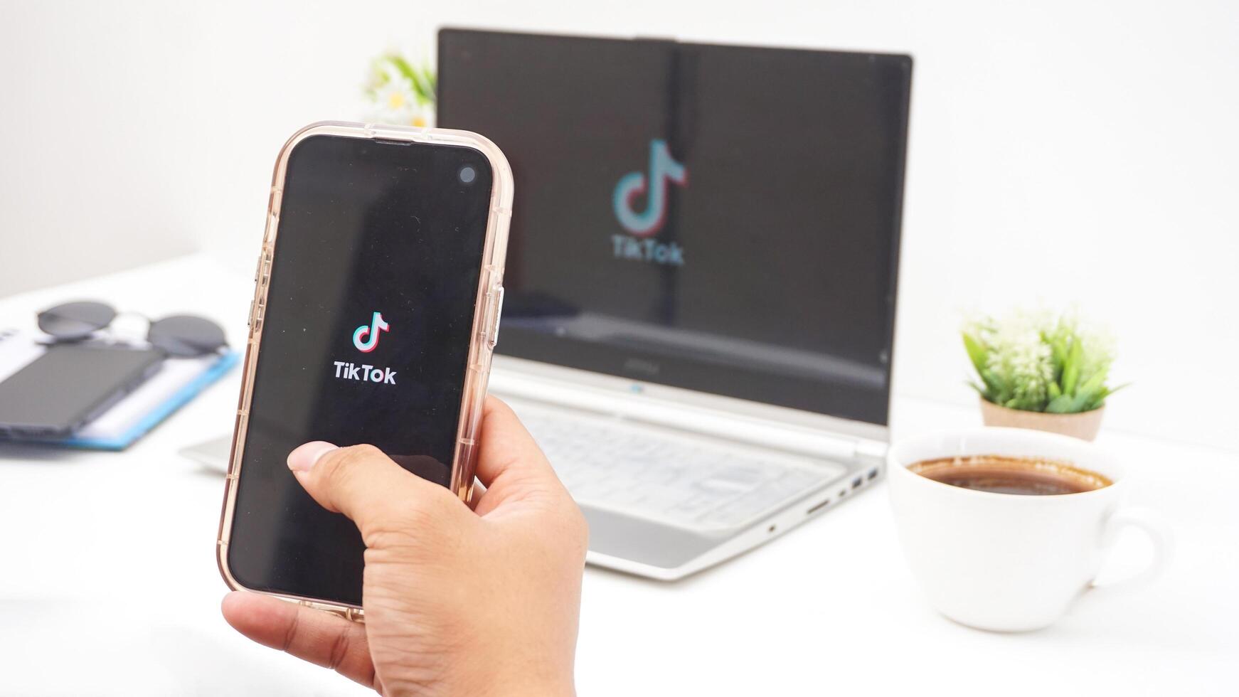 Yogyakarta, Indonesia, 2025 - Hand holding smartphone that shows front page of Tiktok, social and entertainment platform application on the screen isolated on white background photo