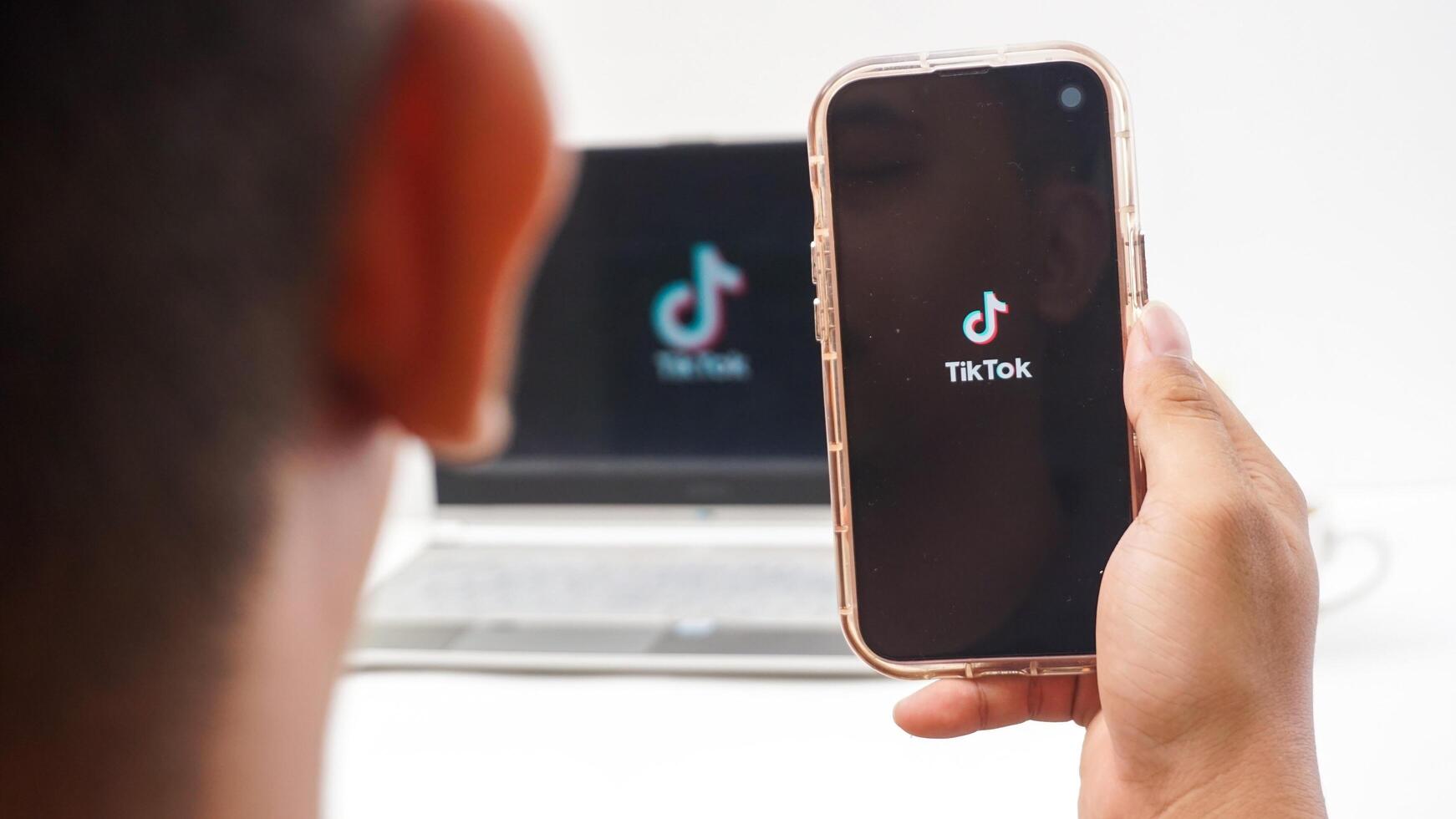 Yogyakarta, Indonesia, 2025 - Man holding smartphone that shows front page of Tiktok, social and entertainment platform application on the screen isolated on white background photo