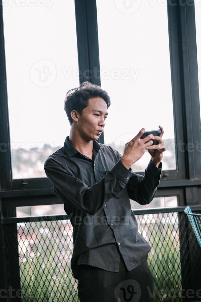 Young man intensely focused on mobile gaming by modern windows photo