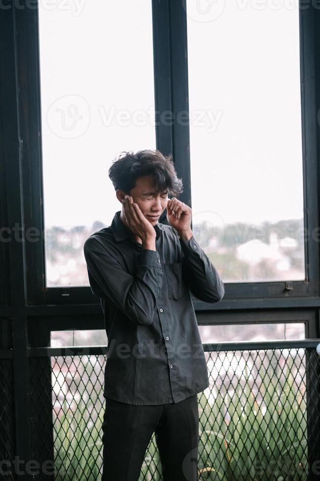 Young man expressing sadness, holding face in despair near window photo