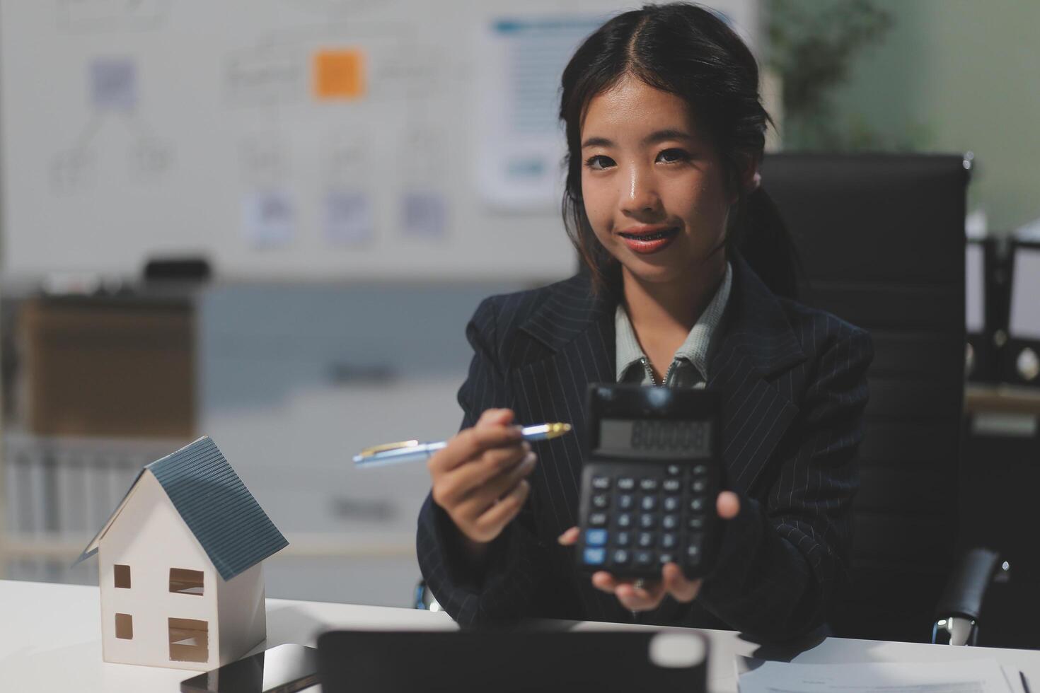A woman in a business suit holding a calculator and a house photo
