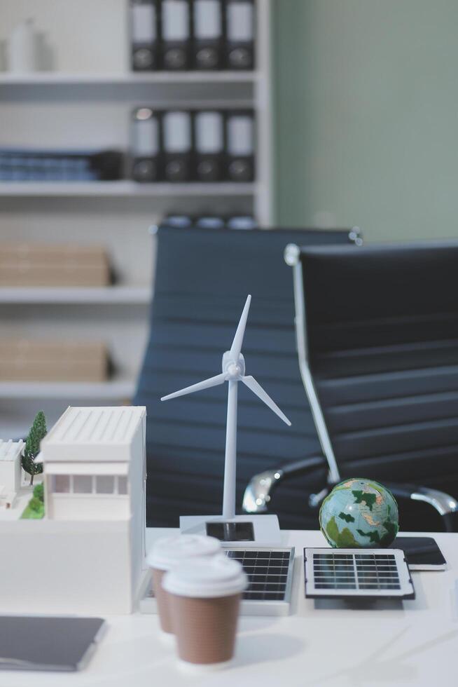 A desk with a laptop, a coffee cup, a wind turbine and a globe photo