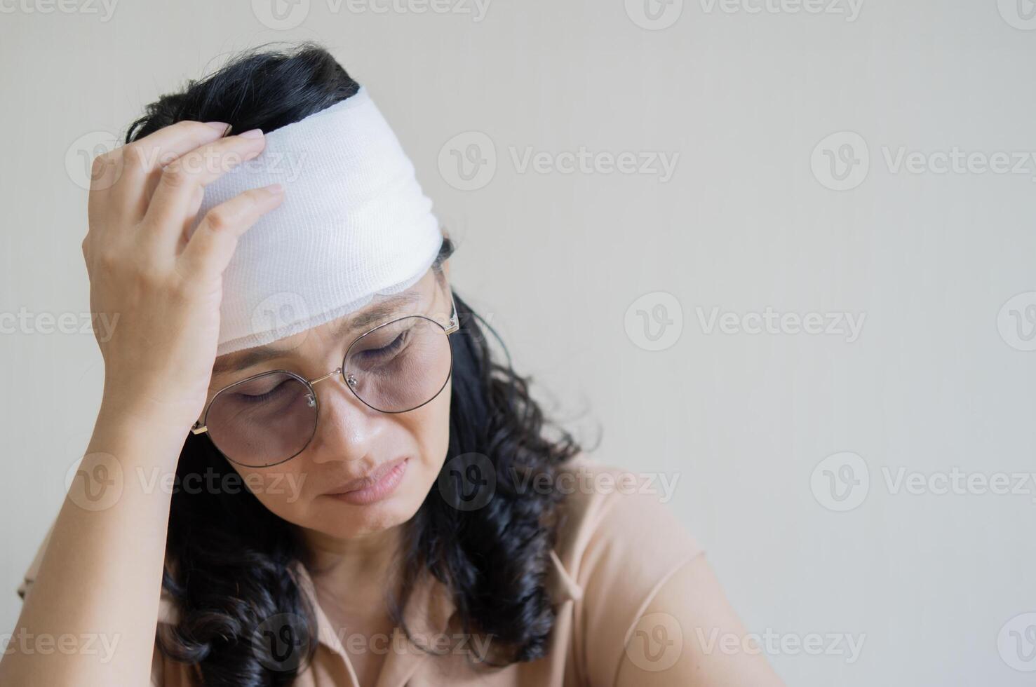 Sad emotional senior Asian woman had serious accident and wears bandage around injured head. photo