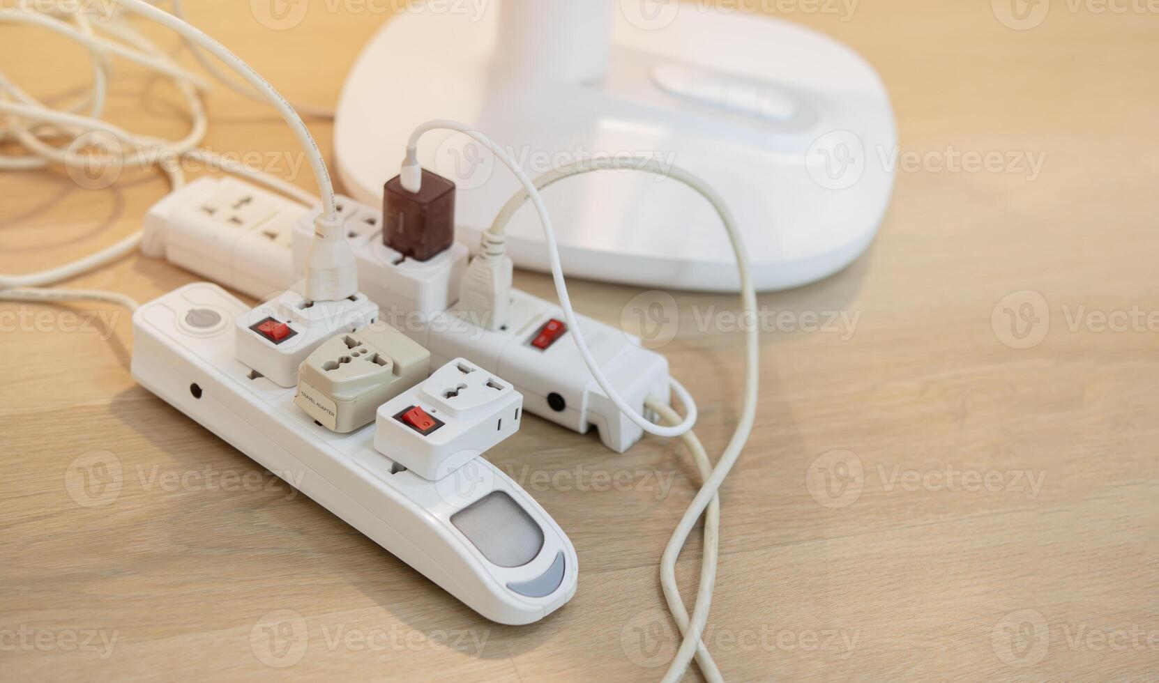 Messy outlet power extension cord on an apartment floor with various charging devices photo