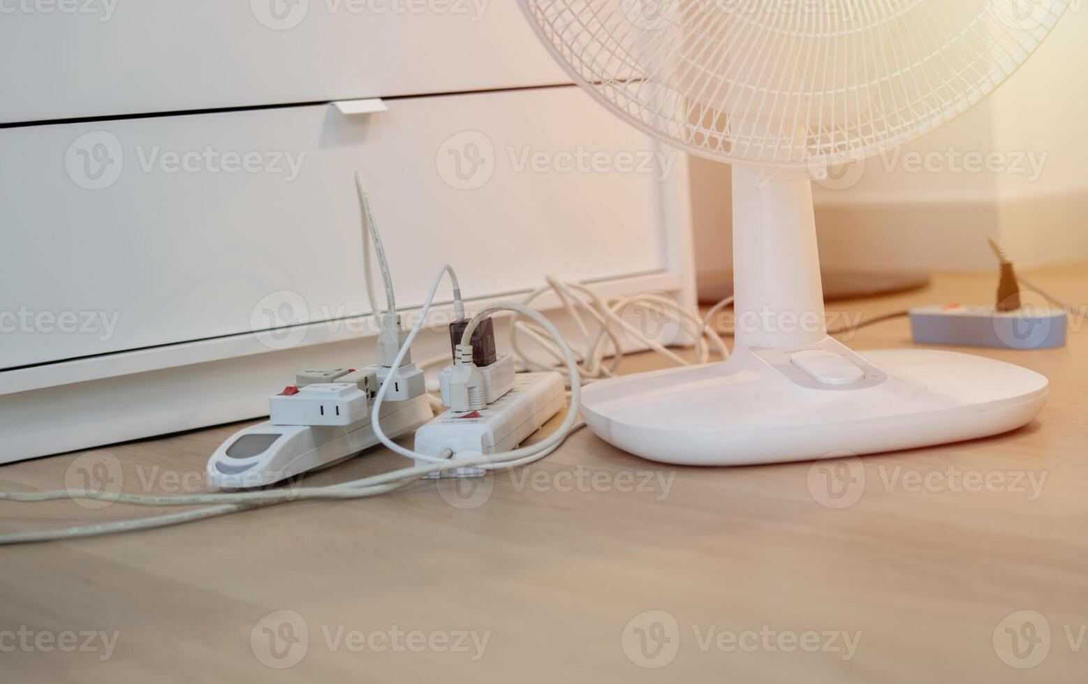 Overloaded power boards with electric fan on wooden floor at home. photo