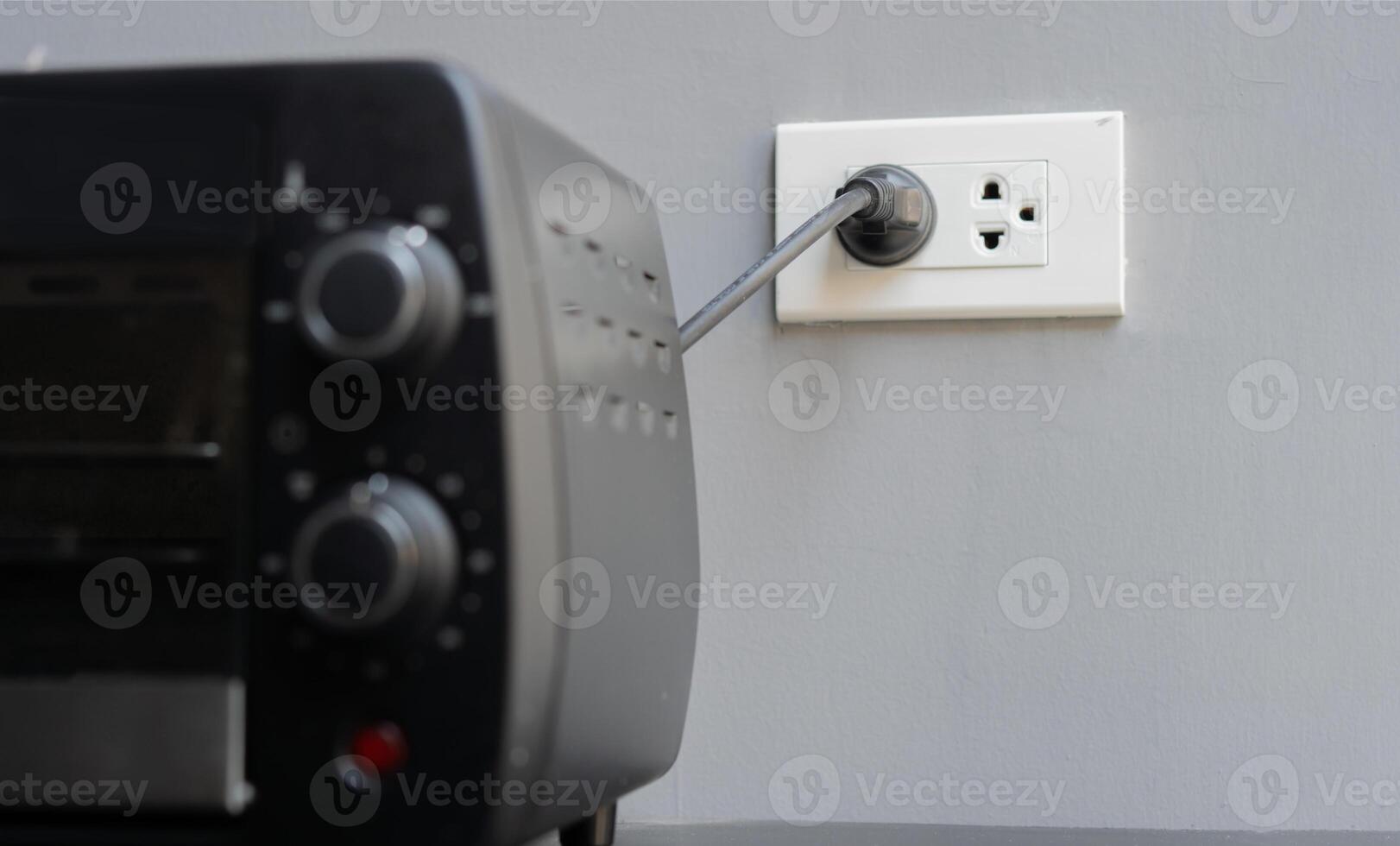 Shot image of black mini electric oven with plugin outlet power at wall background. photo