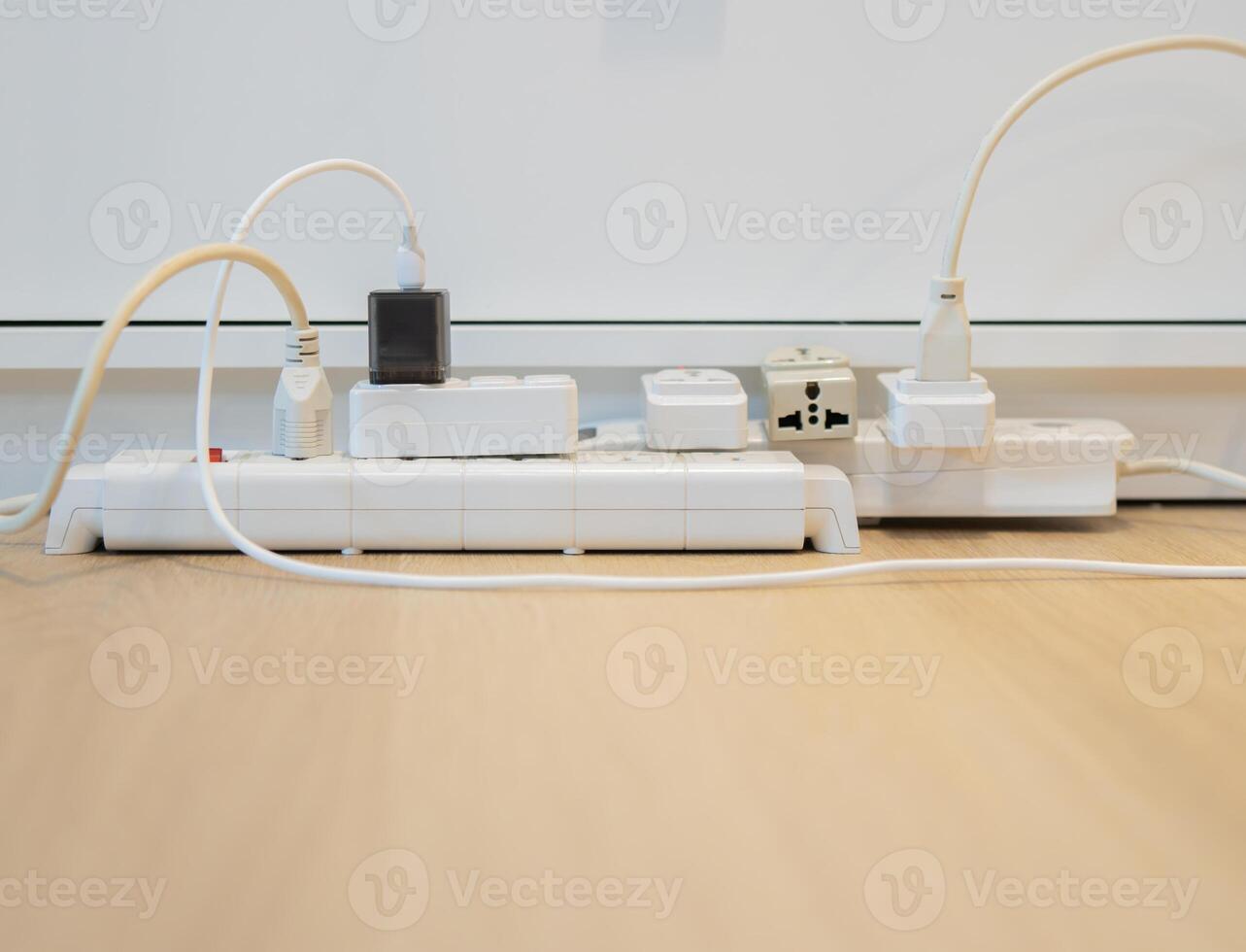 Side view of multiple electrical plugs on wooden floor near by the white sideboard cabinet. photo