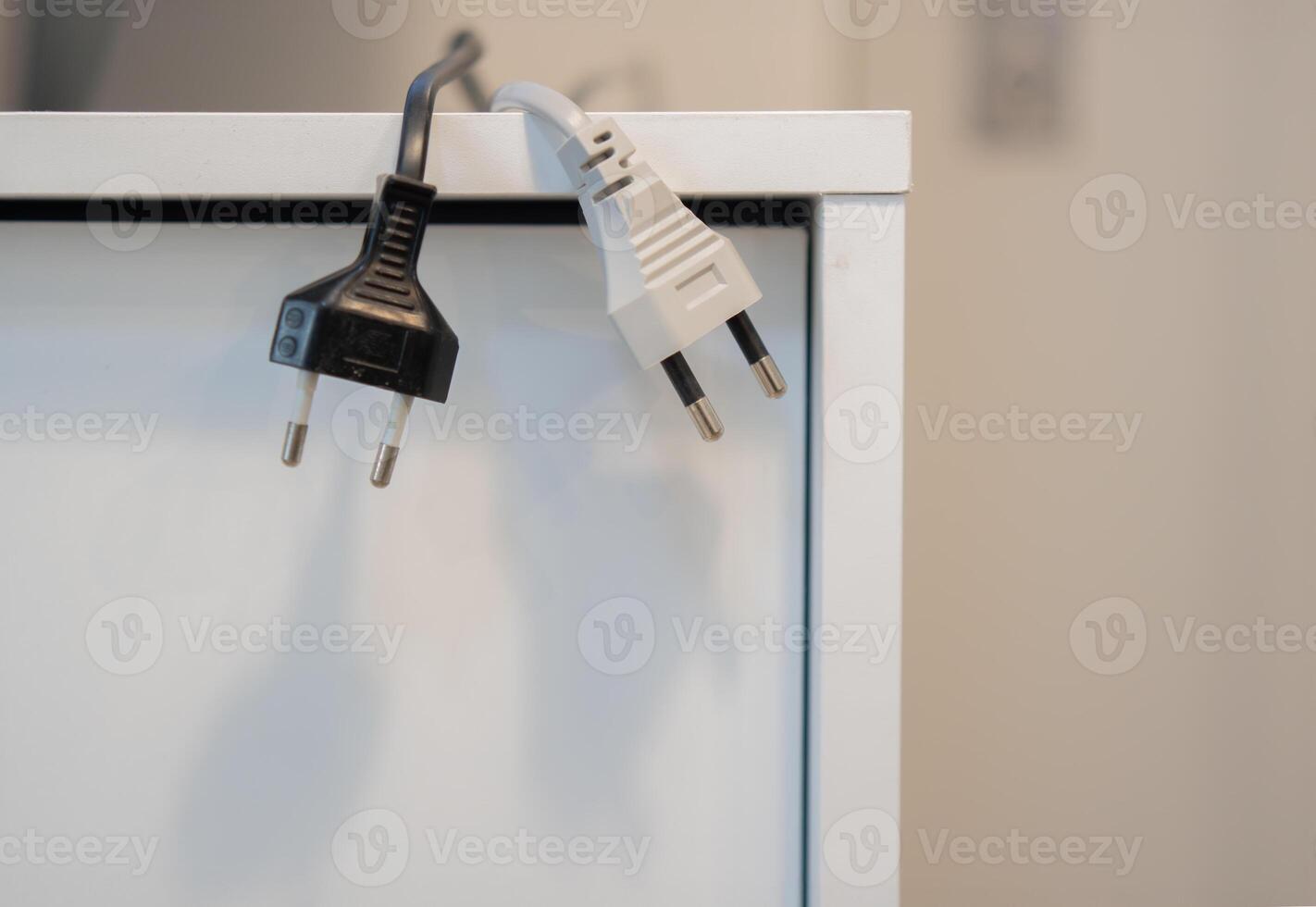 Black and white electric plugs hanging from the sideboard cabinet at office. photo