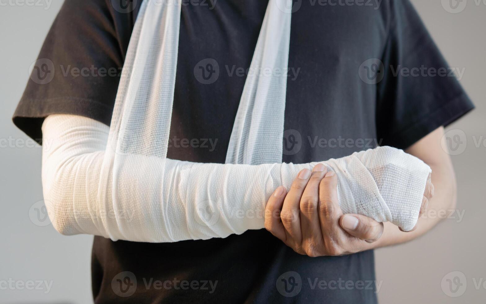 Close-up of man with bandaged hand and arm support standing over light gray color background. photo