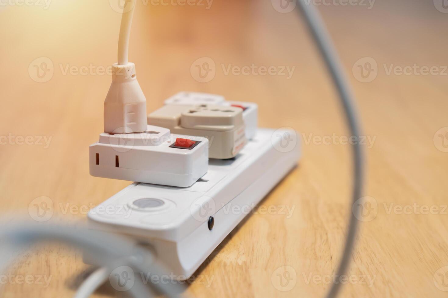 An electric plugged into maltiple electrical outlet on wooden table. Concept of electricity consumption. photo