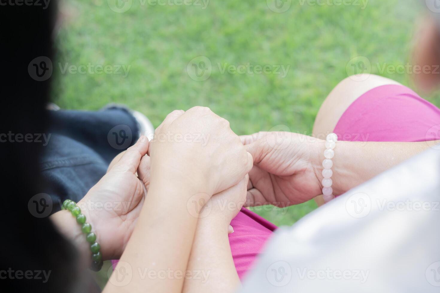 Back view of mother and daughter sit and holding hands while relaxing at park. photo