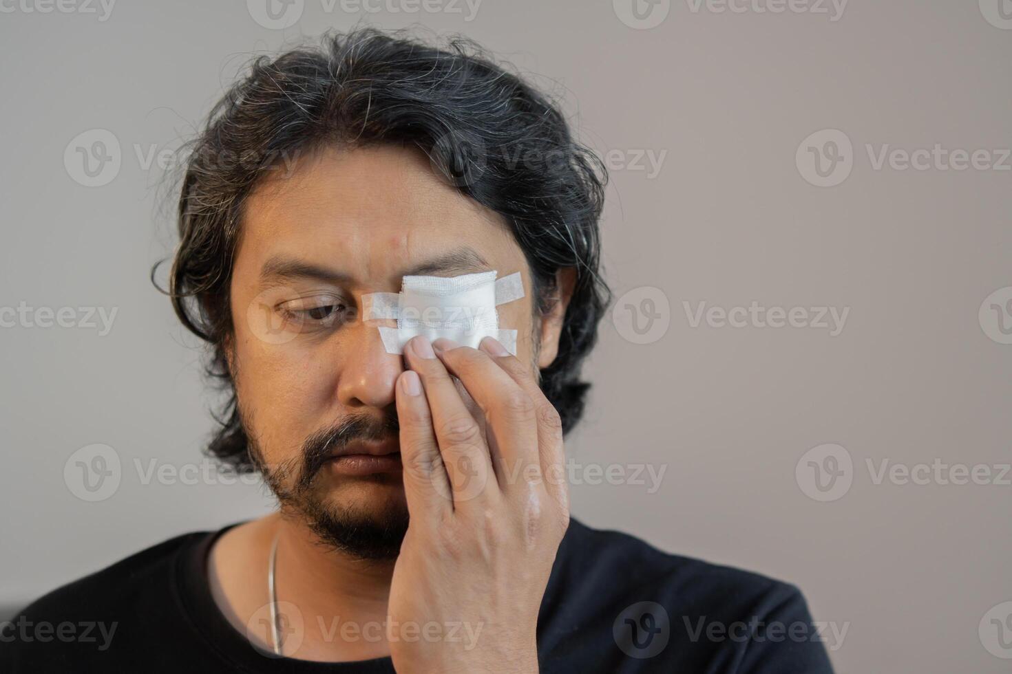 Eye injury, a man has a blindfolded bandaged eye with a white bandage over light gray blackground. photo
