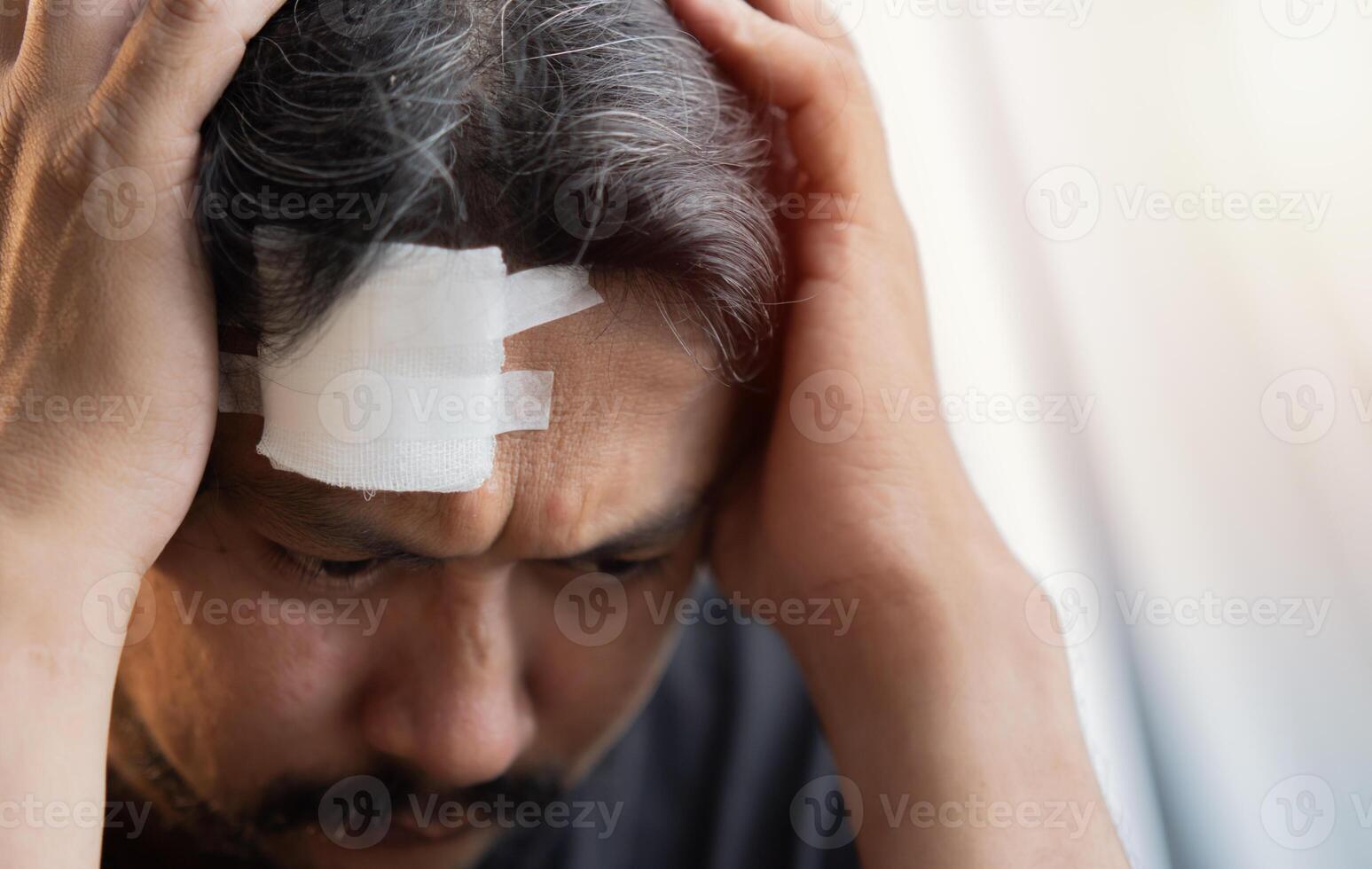 A serious Asian man has a headache and is worried from a wound on his forehead. photo