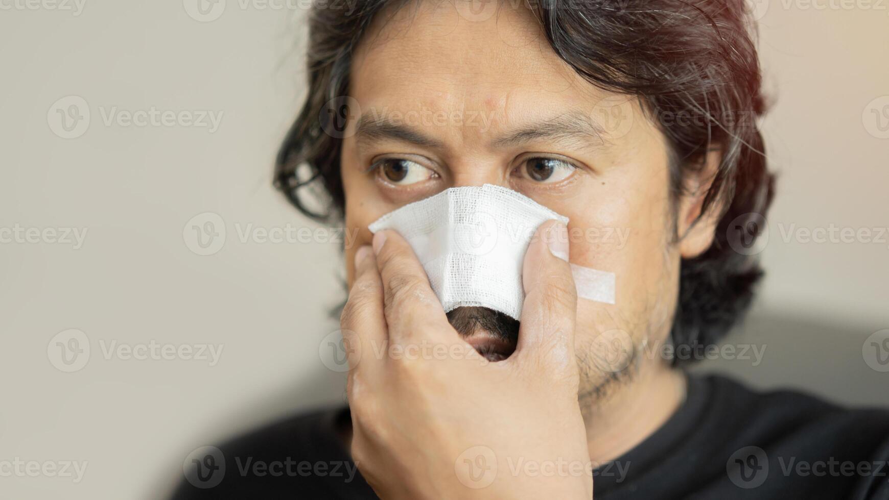 Adult Asian man having a nasal bandage, over soft beige color background with copy space. photo
