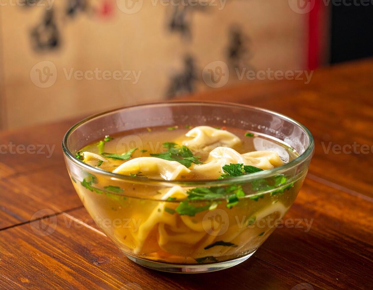 Flavorful Wonton Soup with Dumplings and Herbs in a Clear Bowl on a Wooden Table photo