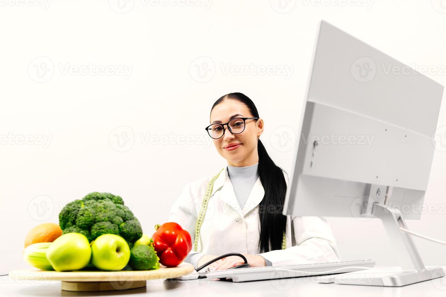 A young female nutritionist points out fresh fruits and vegetables. Broccoli, apple, avocado, celery, peppers, orange. Concept of the importance of healthy eating photo